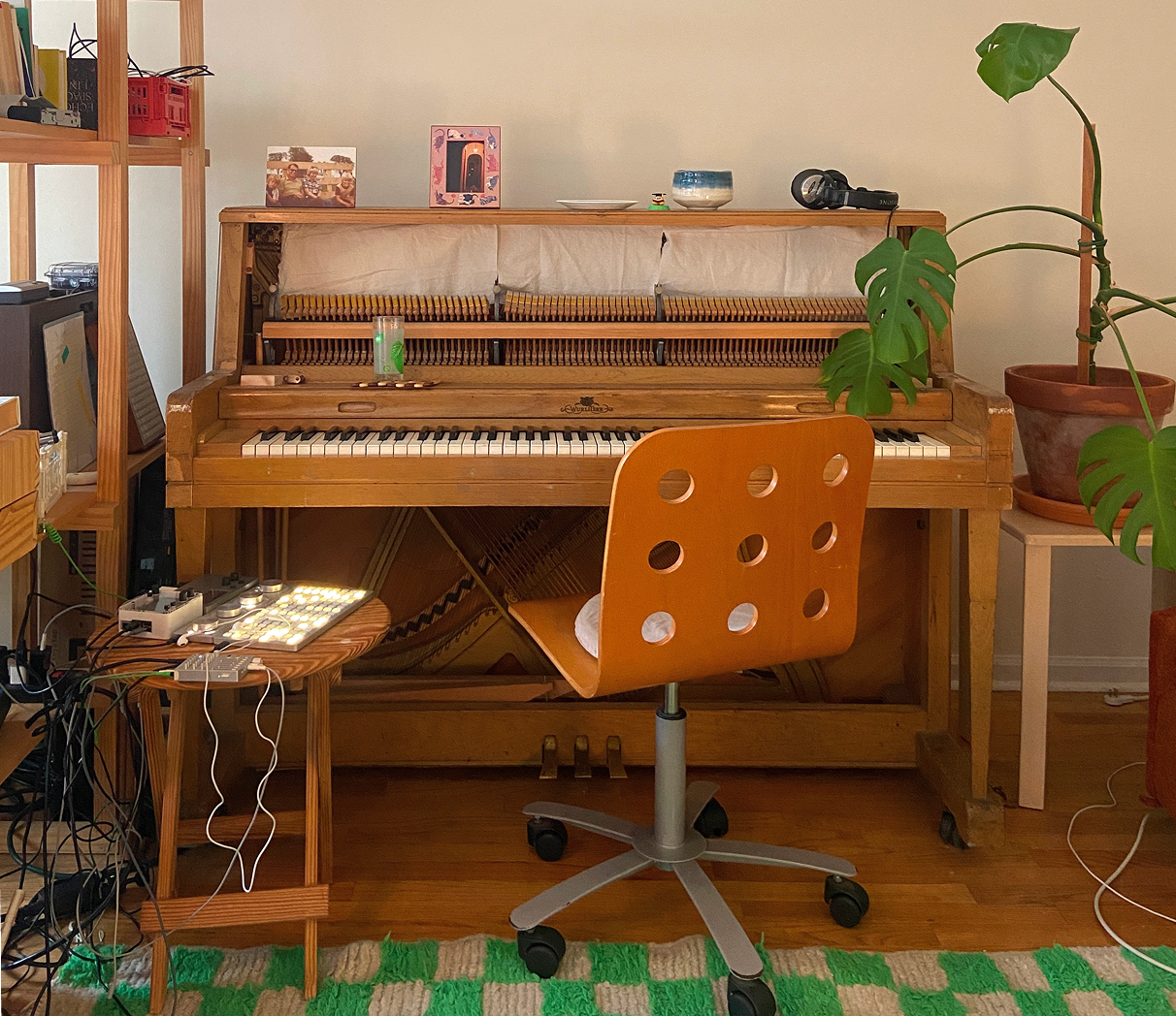 A photo of a piano in a cozy room surrounded by a plant, some electronic music equipment  and wooden furniture